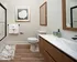 Modern apartment bathroom with wood accents, white countertop, glass shower, and decorative wall art.