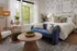 Stylish Montgomeryville apartment bedroom with a blue velvet sofa, wooden coffee table, plush bed, and large windows with greenery.