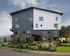 Modern three-story apartment building with stylish facade, lush landscaping, and large windows, offering a perfect blend of contemporary design and natural charm.