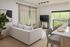 Bright and modern living room with cozy white sofa, sleek flat-screen TV, and expansive glass doors leading to lush greenery, perfect for relaxation and entertainment.