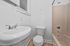 Bright bathroom featuring a modern sink, sleek toilet, and a classic tub with gleaming fixtures, highlighted by fresh white walls and warm wood-style flooring.
