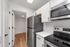 Modern kitchen with sleek stainless steel appliances, white cabinetry, and elegant hardwood flooring leading to a spacious pantry.
