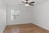 Modern bedroom with elegant wood flooring, large window with blinds, and a sleek ceiling fan, offering ample natural light and a spacious ambiance.
