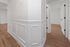 Inviting hallway with elegant wainscoting and sleek wood flooring leading to bright rooms.