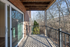 Charming private balcony with a serene wooded view, featuring elegant metal railings and warm wooden overhead, perfect for relaxation.