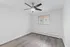 Bright, empty room with sleek wooden flooring, modern ceiling fan, and a large window offering natural light.