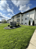 Charming apartment building with lush green lawns and well-maintained landscaping under a bright blue sky.