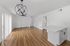 Bright and modern open-concept living area with sleek wood floors and stylish chandelier, adjacent to a spacious white kitchen island.
