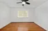 Bright and airy empty room with polished hardwood floors, modern ceiling fan, and large window offering natural light, perfect for a cozy bedroom or home office.