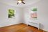 Bright and airy empty room with hardwood floors, two windows offering a green view, and a modern ceiling fan.