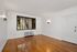 Bright and inviting living room with polished hardwood floors, large window for natural light, and classic wall sconces.