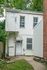 Charming two-story white house with a quaint entrance, nestled between greenery and brickwork, offering a cozy and private living space.