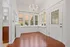 Bright and inviting corner space with elegant chandelier, large windows, and polished wood flooring, perfect for dining or relaxation.