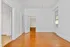 Bright and spacious room with elegant hardwood floors, white walls, and an open doorway revealing patterned wallpaper in the next room.