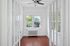 Bright sunlit room with large windows, elegant French doors, and a sleek ceiling fan, ideal for a cozy retreat or home office.