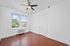 Bright and airy room with polished hardwood floors, large windows offering lush greenery views, and a modern ceiling fan for comfort.