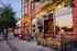 Charming urban street with vibrant storefronts and outdoor seating at dusk.