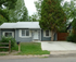 Quaint single-story gray house with a white roof, front porch, and lush green surroundings.