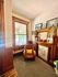 Inviting corner with a wicker chair, decorative fireplace, and natural light streaming through a tall window.