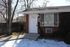 Cozy brick home with large front window, surrounded by trees and a wooden fence.