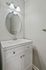 Modern bathroom with elegant lighting, sleek oval mirror, and chic white vanity offering ample storage.