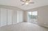 Bright and airy bedroom with plush carpeting, featuring a ceiling fan, dual closets, and access to a private balcony with scenic outdoor views.