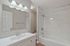 Elegant bathroom featuring a sleek white vanity, large mirror with modern lighting, and a pristine bathtub with a marble accent wall.