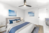 Elegant bedroom with chic decor, featuring a plush bed with blue and white bedding, modern ceiling fan, and serene ocean-themed artwork on the walls.