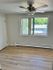 Bright and airy room with modern ceiling fan, large window offering a scenic view, and sleek hardwood flooring.