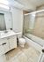 Modern bathroom with sleek white vanity, elegant mirror, and luxurious glass-enclosed shower over tub, featuring bright tiles and contemporary fixtures.