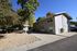 Charming duplex with modern exterior nestled among lush trees, featuring a well-maintained yard and convenient parking.