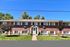 Charming brick apartment building with well-maintained lawn and mature trees under a clear blue sky.