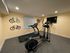 Charming home gym with modern treadmill, elliptical machine, and wall-mounted cycles, featuring cozy ambiance and stylish decor.