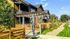 Charming multi-story apartments with wooden accents, lush landscaping, and inviting pergola entryway under a clear blue sky.