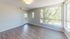 Bright living room with large windows offering a scenic view of lush greenery, featuring elegant wood flooring and modern light fixture.