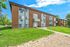 Charming brick apartment building with modern accents, surrounded by lush green lawns and a clear blue sky.