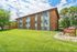 Charming Peakview Apartments exterior showcasing a beautifully maintained lawn, lush trees, and a welcoming atmosphere under a bright blue sky.