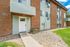 Charming brick and siding apartment exterior with modern double doors, framed by lush green lawns and decorative stone pathways.