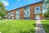 Charming brick apartment complex with modern siding, surrounded by lush green lawn under a bright blue sky.