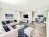 Elegant living room with modern decor, featuring a plush cream sofa, stylish blue cushions, a chic coffee table, and a tastefully minimalistic dining area.