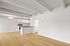 Elegant open-plan space with light wood flooring and modern kitchen featuring sleek countertops and white cabinetry.