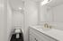 Elegant and modern bathroom featuring a pristine white vanity with stylish gold fixtures, a large mirror, and a sleek shower area.