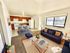 Bright and inviting living room with a modern kitchen and dining area, featuring a cozy navy sofa, stylish copper accents, and large windows for abundant natural light.
