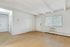Bright and airy living space with sleek wooden floors, white walls, and a large window featuring a view of greenery.