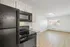 Bright and modern apartment kitchen with sleek black appliances and open living space featuring abundant natural light from large windows.