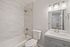 Elegant modern bathroom featuring marble tile shower, sleek vanity with ample lighting, and a spacious bathtub.