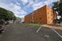 Charming brick apartment building with ample parking, surrounded by lush greenery under a bright blue sky.