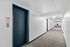 Modern apartment hallway with clean white walls, sleek blue elevator door, and bright overhead lighting.