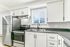 Contemporary kitchen featuring sleek stainless steel appliances, elegant white cabinetry, and a sunlit window view.