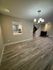 Elegant living space with sleek wooden floors, modern chandelier, and a peek into a contemporary kitchen.